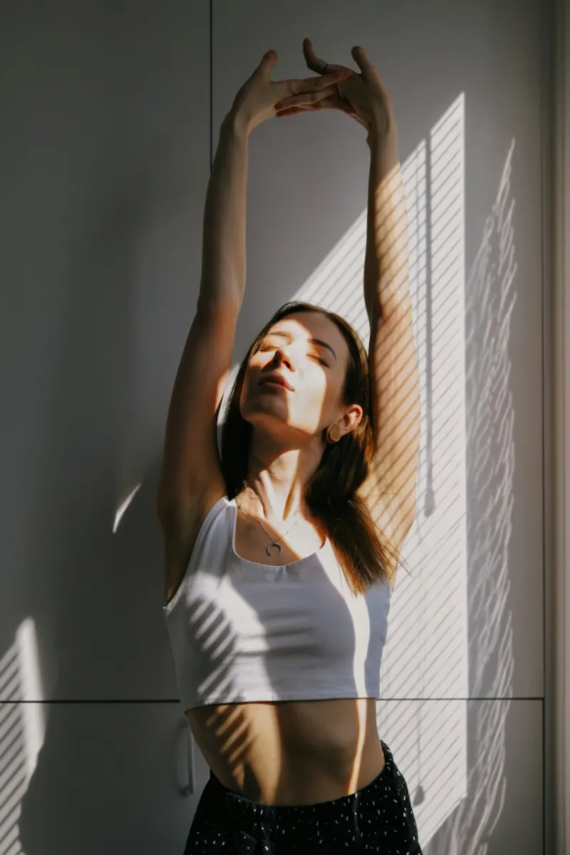 Femme qui s'étire bras levés dans la lumière du matin
