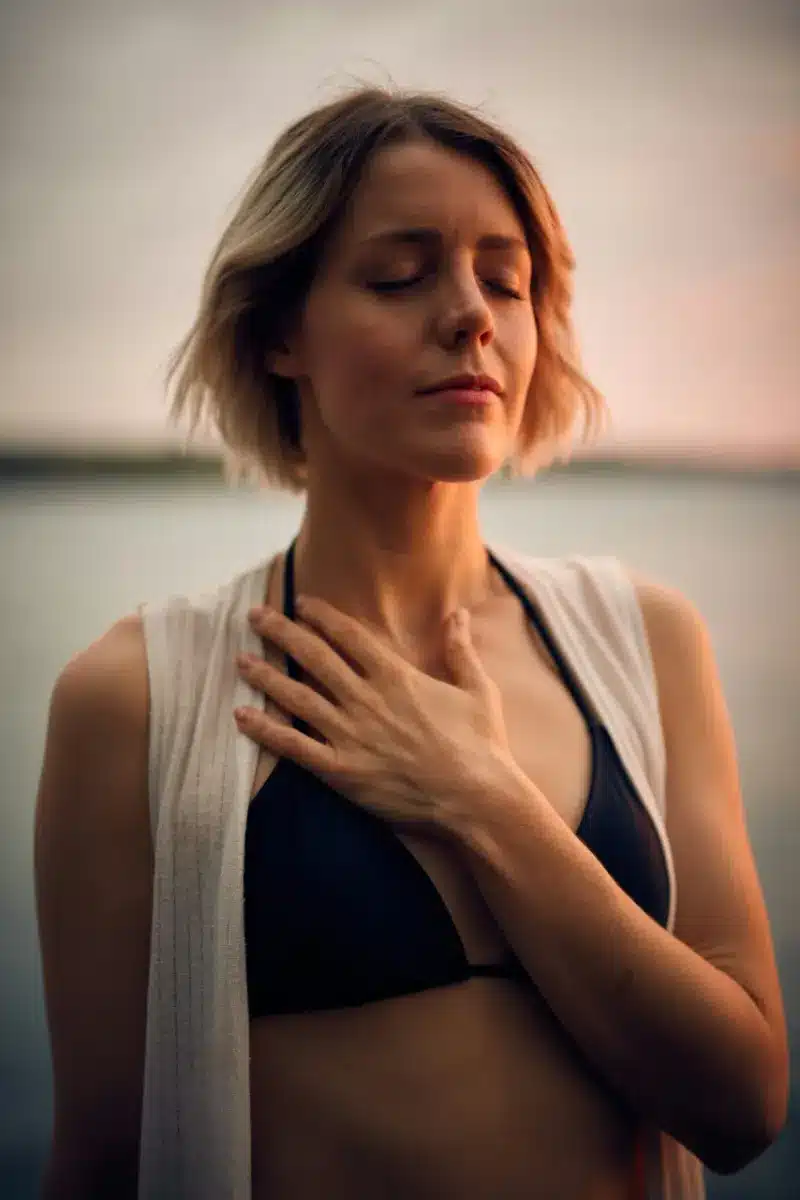 Femme les yeux fermés, main sur la poitrine, au coucher du soleil