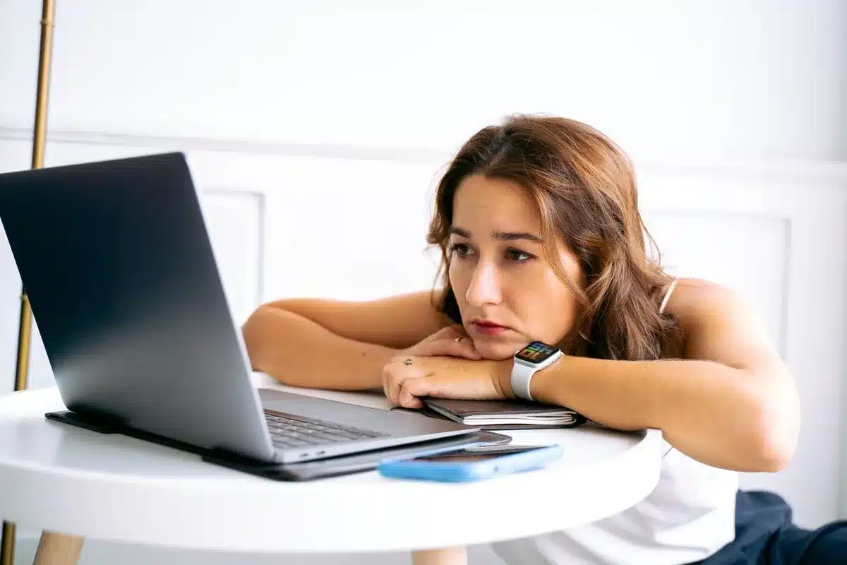 Une femme appuyée sur ses bras devant un ordinateur portable, le regard fatigué