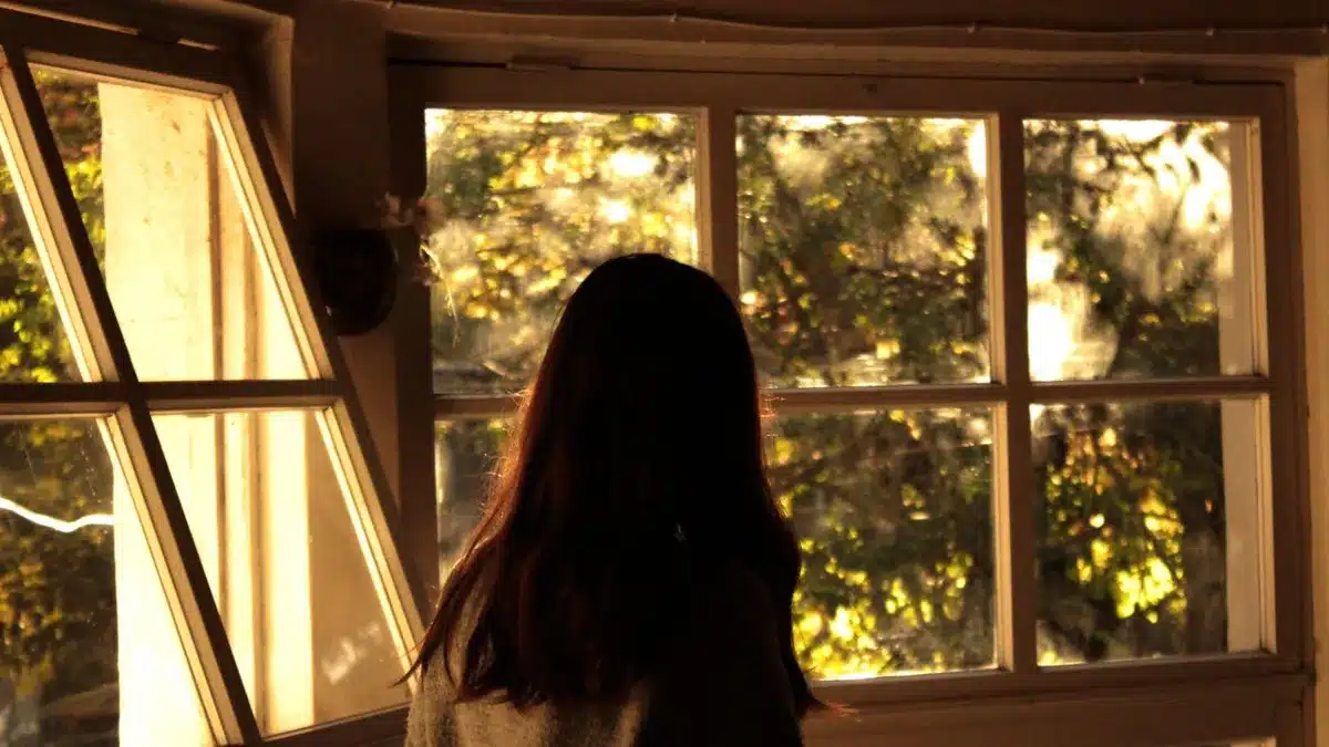 Femme de dos devant une grande fenêtre qui laisse entrer une lumière d’automne dorée