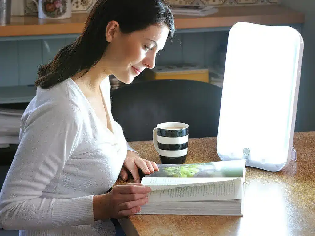Femme lisant à une table devant une lampe de luminothérapie allumée