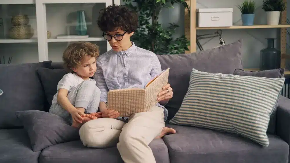 Une mère assise sur un canapé lit un livre à son jeune enfant
